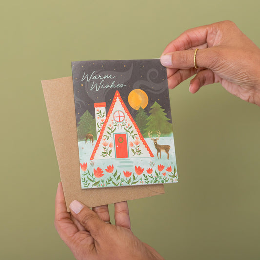 Warm Winter Cabin Christmas greeting card held in hand