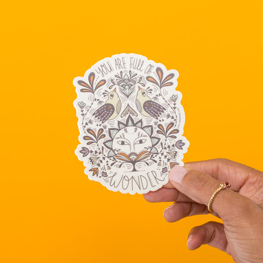Full of Wonder vinyl sticker held in hand, encouraging message with folk-art sun and birds by Amita Nair