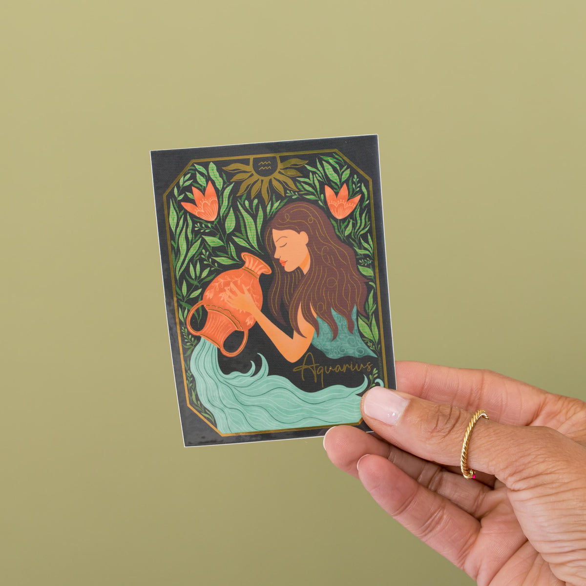 Aquarius zodiac vinyl sticker held in hand, water bearer with gold metallic accents and coral florals by Amita Nair