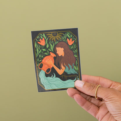 Aquarius zodiac vinyl sticker held in hand, water bearer with gold metallic accents and coral florals by Amita Nair