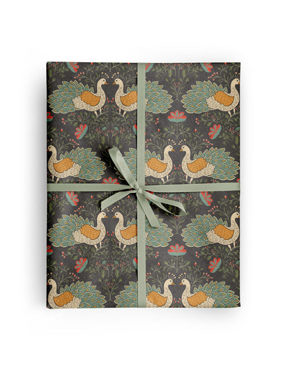 Peacock Garden Wrapping Paper wrapped around a gift, hand-illustrated cream and teal peacocks with coral blooms on deep charcoal by Amita Nair